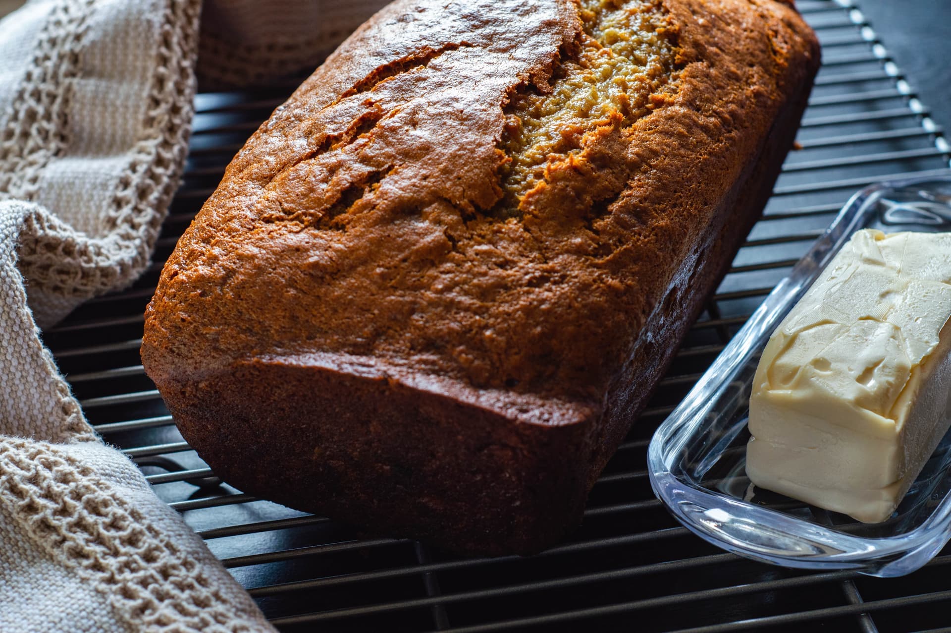 Vegan banana bread loaf on cooling rack with butter