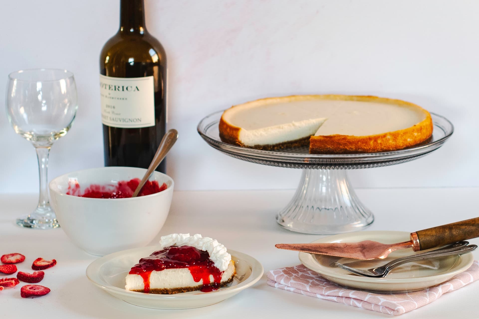 Vegan cheesecake on glass cake stand with wine bottle and jam