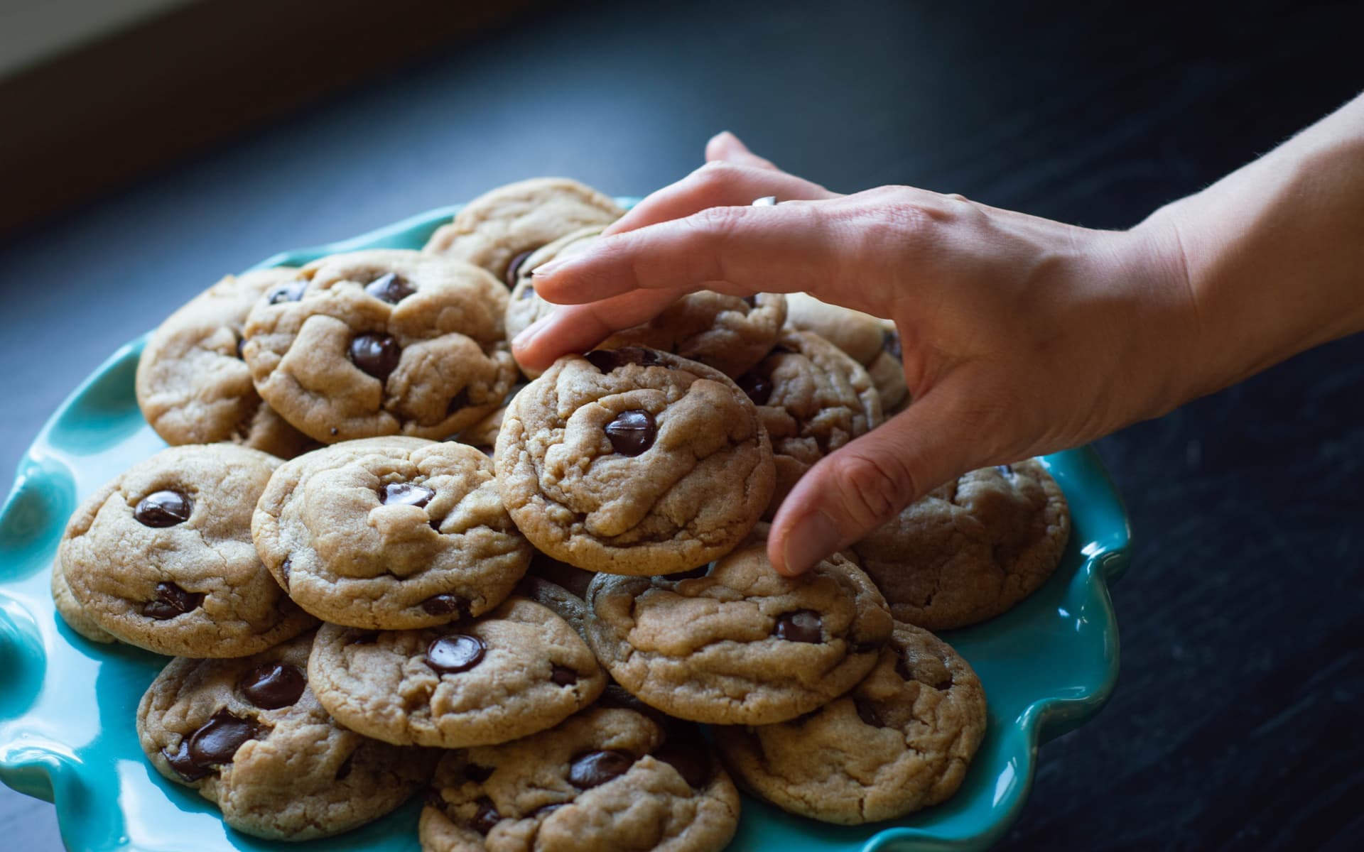 Hand reaching for chocolate chip cookies on turquoise plate