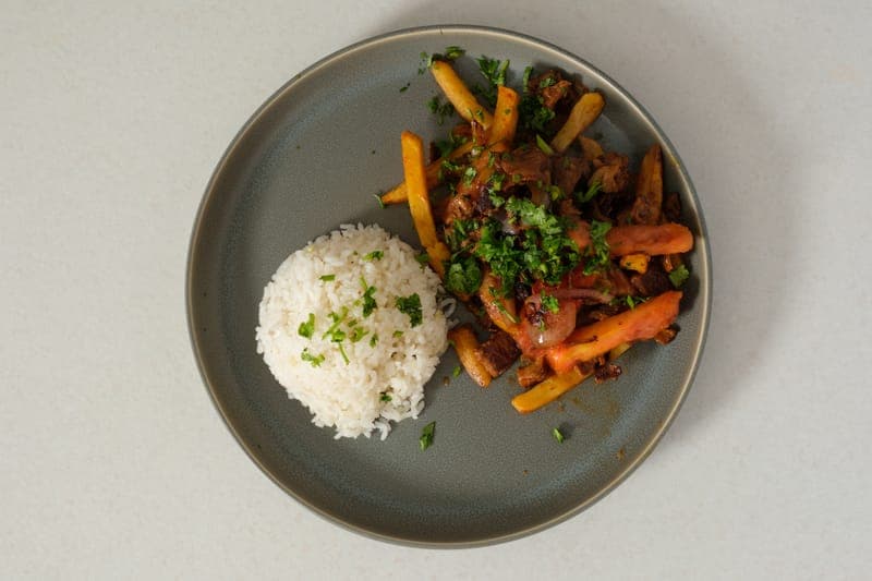 Vegan Lomo Saltado plated with rice and fries